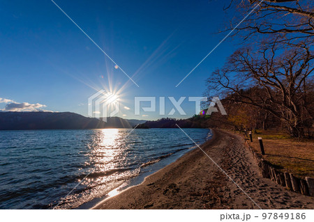 春の青森県・十和田湖で見た、太陽に照らされる湖岸沿いの風景と夕暮れが迫る青空 97849186