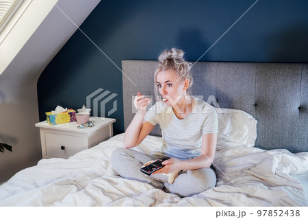 Frustrated woman in home clothes eating ice cream, using the remote control to change the channel while glazing TV in bed during day. Overeating, Jamming of negative emotions. Selective focus. Frustrated woman in home clothes eating ice cream, using the remote control to change the channel while glazing TV in bed during day. Overeating, Jamming of negative emotions. Selective focus. 97852438