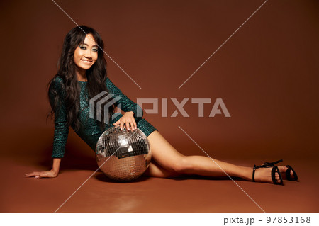 Pretty woman in sequin party gown posing on floor with disco ball 97853168