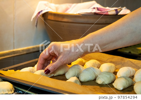 A woman's hand puts small raw pies in a pan. Meat pies are traditional Latvian holiday dishes. A woman's hand puts small raw pies in a pan. Meat pies are traditional Latvian holiday dishes. 97854294
