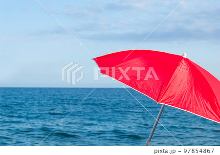 Red parasol umbrella on tropical island beach. Colourful sunshade in the beach on sunny summer day. Holiday relaxation with turquoise sea and blue sky landscape. Summer vacation concept 97854867