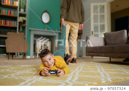 Portrait of smiling son playing video game while father pulling him out 97857324