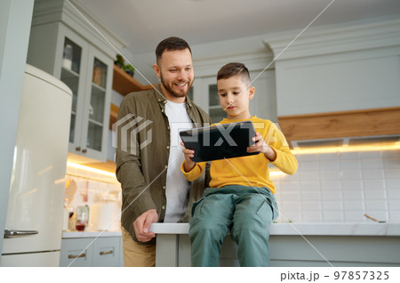 Father with son using digital tablet together at home kitchen 97857325