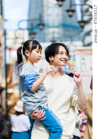 大阪観光で通天閣を背に名物の串かつを食べる親子 97858317