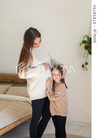 Cute little girl listening to baby's moves in pregnant moms belly Cute little girl listening to baby's moves in pregnant moms belly 97858791