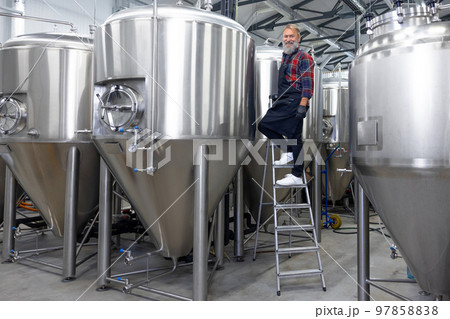Factory worker checking the tanks with beer and looking satisfied with the result 97858838