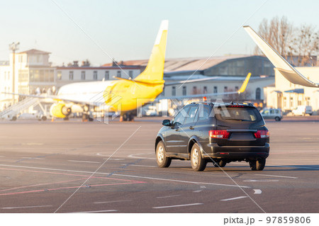Scenic view of airport security car on tarmac apron taxiway in warm sunlight of bright morning sunrise or evening sunset time. Follow me safety vehicle staff. Aviation maintenance and service machine Scenic view of airport security car on tarmac apron taxiway in warm sunlight of bright morning sunrise or evening sunset time. Follow me safety vehicle staff. Aviation maintenance and service machine 97859806
