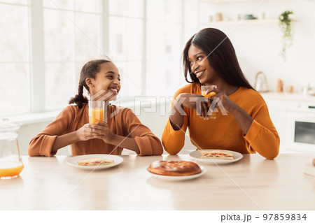 African Mommy And Daughter Having Lunch Drinking Juice In Kitchen African Mommy And Daughter Having Lunch Drinking Juice In Kitchen 97859834