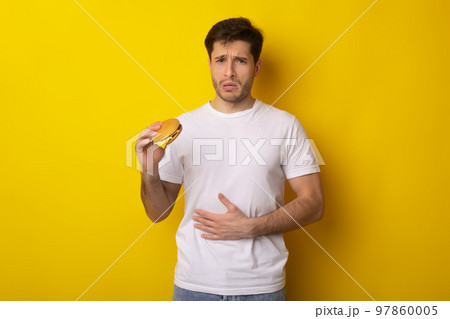 Sad Young Guy Holding Burger Suffering From Stomachache Sad Young Guy Holding Burger Suffering From Stomachache 97860005