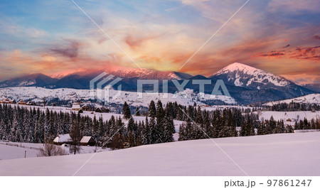 Alpine village outskirts panorama in last evening sunset sun light. Winter snowy hills and fir trees, magnificient and picturesque mountain range in far. Voronenko, Ukraine, Carpathian. Alpine village outskirts panorama in last evening sunset sun light. Winter snowy hills and fir trees, magnificient and picturesque mountain range in far. Voronenko, Ukraine, Carpathian. 97861247