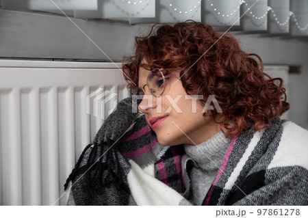 A girl huddled around a hot radiator. The first start of the central heating system. 97861278