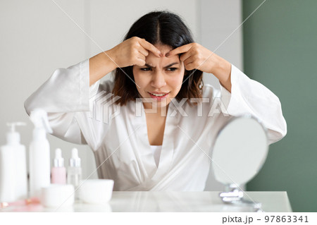 Irritated young woman suffering from acne, pop pimples 97863341