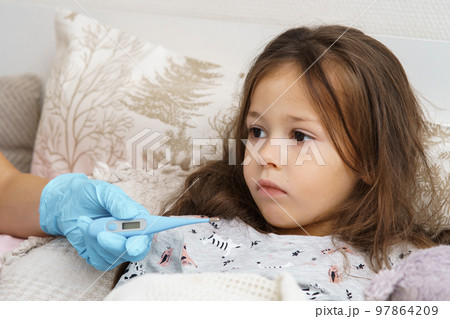 Doctor hand in medical glove measure temperature of sick little girl with electronic thermometer. Fever heat, bed rest. Doctor hand in medical glove measure temperature of sick little girl with electronic thermometer. Fever heat, bed rest. 97864209