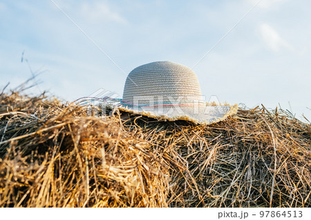 Wicker female panama hat lying at top of haystack. Beautiful clear blue sky. Pile of dry grass. Countryside lifestyle. Wicker female panama hat lying at top of haystack. Beautiful clear blue sky. Pile of dry grass. Countryside lifestyle. 97864513