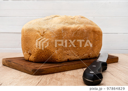 Homemade bread last made with a bread machine on a wooden board with a bread knife. Space for text. Homemade bread last made with a bread machine on a wooden board with a bread knife. Space for text. 97864829