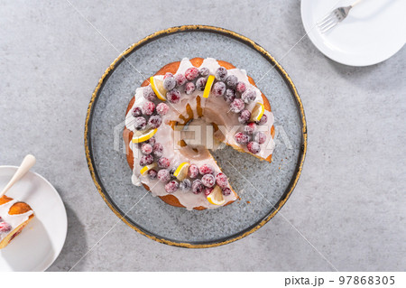 Flat lay. Sliced lemon cranberry bundt cake decorated with sugar cranberries and lemon wedges on a cake stand. 97868305