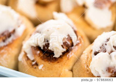 Freshly baked cinnamon rolls with white icing in a blue baking pan. 97868663