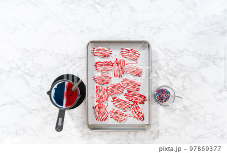 Flat lay. Drizzling melted chocolate over chocolate-dipped pretzels twists. 97869377