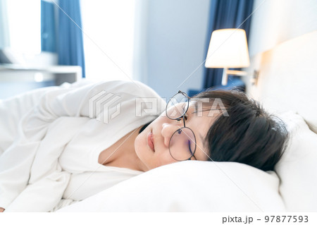 Asian young woman is sleepping on white clean bed in white t-shirt long arm pajamas and in spite of wear glasses on her eyes. 97877593