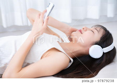 フローリングに寝転んでスマホ音楽を聴く女性 97879238