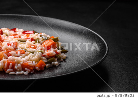 Delicious fresh risotto with vegetables, spices and herbs on a black plate Delicious fresh risotto with vegetables, spices and herbs on a black plate 97879803