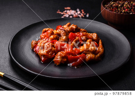Delicious juicy meat with hot peppers and sauce on a black ceramic plate Delicious juicy meat with hot peppers and sauce on a black ceramic plate 97879858