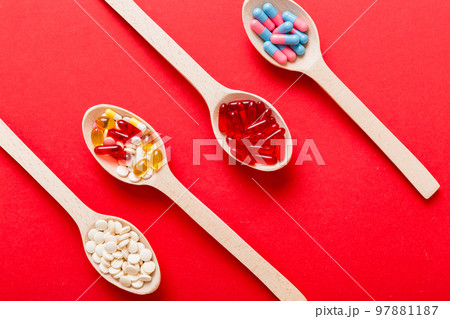 Vitamin capsules in a spoon on a colored background. Pills served as a healthy meal. Red soft gel vitamin supplement capsules on spoon 97881187