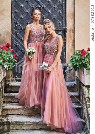 Beautiful bridesmaids in gorgeous elegant stylish red pink violet floor length v neck chiffon gown dress decorated with sequins sparkles and rhinestones holding flowers bouquets. Wedding day in old 97882913