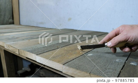 filling up holes and cracks on a wooden surface with a narrow trowel in a man's hand, patching up irregularities on a structure made of rough boards in a workshop or garage close-up 97885785
