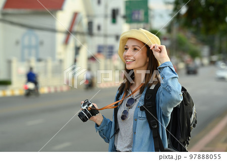 Young female tourist with backpack and digital camera standing on city street. Blogger, vacation and journey concept 97888055