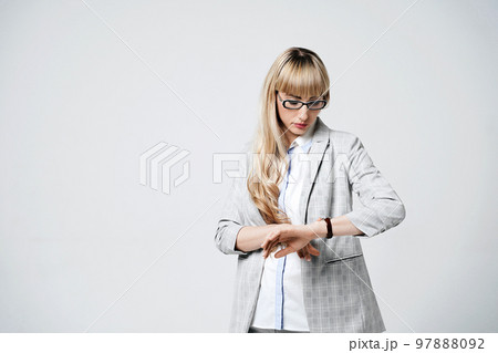 Young beautiful blonde woman in studio on light gray background. Model in pantsuit and glasses checking time with a wristwatch. Young beautiful blonde woman in studio on light gray background. Model in pantsuit and glasses checking time with a wristwatch. 97888092