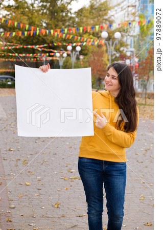 A young Caucasian woman points her finger at a blank sheet of paper and smiles 97889072