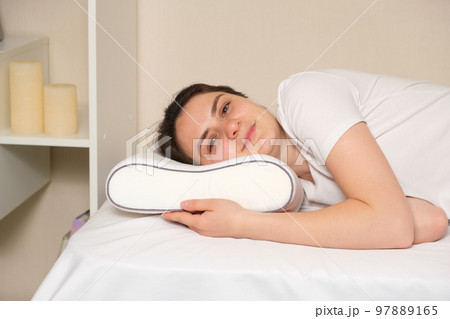 A woman lies on an orthopedic pillow, looks into the camera and smiles. 97889165