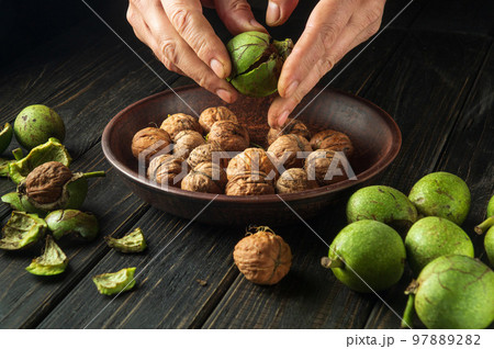 Peeling walnuts from green skins before preparing a culinary dish. Close-up cook hands on the kitchen table 97889282