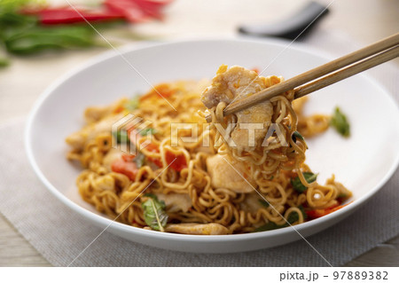 Close up use chopsticks clamp noodles,Spicy stir fried instant noodle with sliced chicken breast and thai basil leaves in white plate 97889382