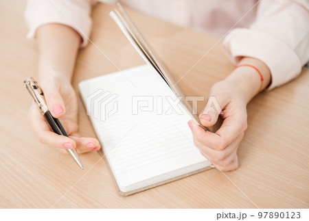 Close up of a woman's hands writing in a notepad placed on a wooden table, home office and work concept, plans and thoughts Close up of a woman's hands writing in a notepad placed on a wooden table, home office and work concept, plans and thoughts 97890123