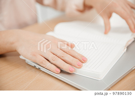 Close up of a woman's hands writing in a notepad placed on a wooden table, home office and work concept, plans and business meeting Close up of a woman's hands writing in a notepad placed on a wooden table, home office and work concept, plans and business meeting 97890130