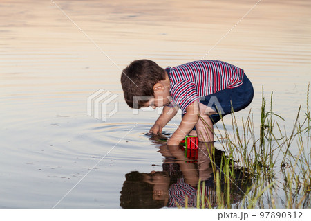 A little boy 2-3 years old plays on the river bank, the reflection of a child in the water. Outdoors in summer. 97890312