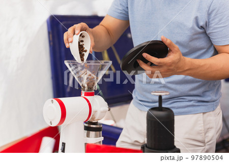 Barista pours coffee beans into the coffee machine grinder to make black coffee. Barista pours coffee beans into the coffee machine grinder to make black coffee. 97890504