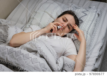 A woman with rhinitis squeaks a saline solution or vasoconstrictor drops into the nose lying in bed, top view. 97890677