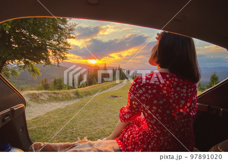 a woman sits in the trunk of a car with a view of the sunset in the mountains 97891020