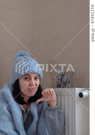 a woman is warming herself by the radiator, she complains that the heat is getting more expensive a woman is warming herself by the radiator, she complains that the heat is getting more expensive 97891159