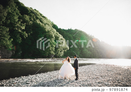 Elegant stylish happy blonde bride and gorgeous groom on the background of a beautiful river in the mountains Elegant stylish happy blonde bride and gorgeous groom on the background of a beautiful river in the mountains 97891874