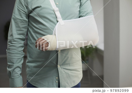 Man wearing a bandage and a sling after the surgery on his arm with a joint dislocation 97892099