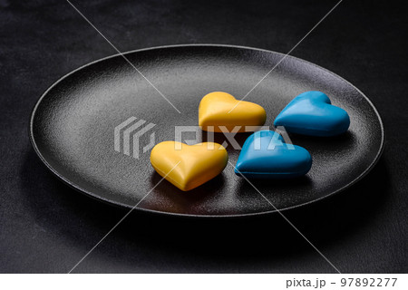 Chocolate hearts in the colors of the Ukrainian flag on a black ceramic plate 97892277