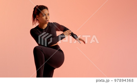 Fitness black woman standing doing elbow to knee crunch, looking aside at free space, neon peach background, panorama Fitness black woman standing doing elbow to knee crunch, looking aside at free space, neon peach background, panorama 97894368