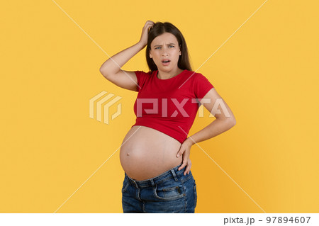 Portrait Of Confused Young Pregnant Woman Scratching Head And Looking At Camera Portrait Of Confused Young Pregnant Woman Scratching Head And Looking At Camera 97894607