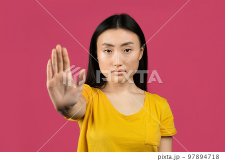 Young japanese lady gesturing STOP, showing rejection gesture, expressing her negative attitude, pink background 97894718