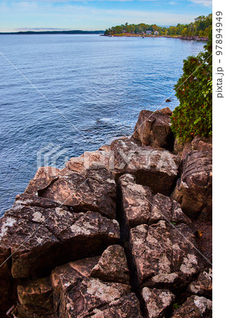Detail of large rocky cliffs on coast with diagonal cuts and houses in distance 97894949