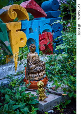Detail of small Buddha statue and colorful letters in garden 97895124